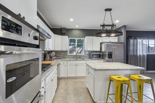 kitchen with appliances with stainless steel finishes, white cabinetry, a wealth of natural light, and tasteful backsplash