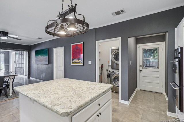 kitchen featuring white cabinets, stacked washer and clothes dryer, a center island, and ceiling fan