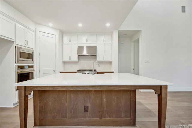 kitchen with a kitchen island with sink, ventilation hood, stainless steel appliances, and white cabinets