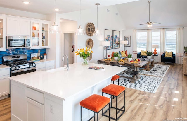 kitchen featuring stainless steel appliances, light wood-type flooring, vaulted ceiling, and white cabinetry