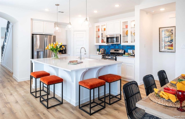 kitchen with a kitchen island with sink, stainless steel appliances, hanging light fixtures, and white cabinetry