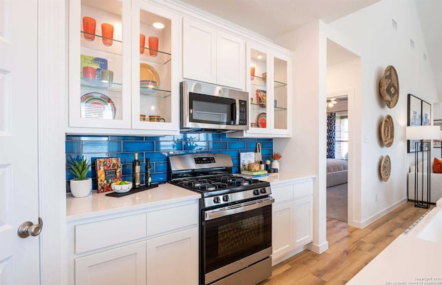 kitchen with white cabinets, appliances with stainless steel finishes, light wood-type flooring, and tasteful backsplash