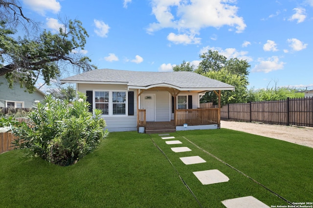 view of front of property with a shingled roof, a front yard, covered porch, and fence