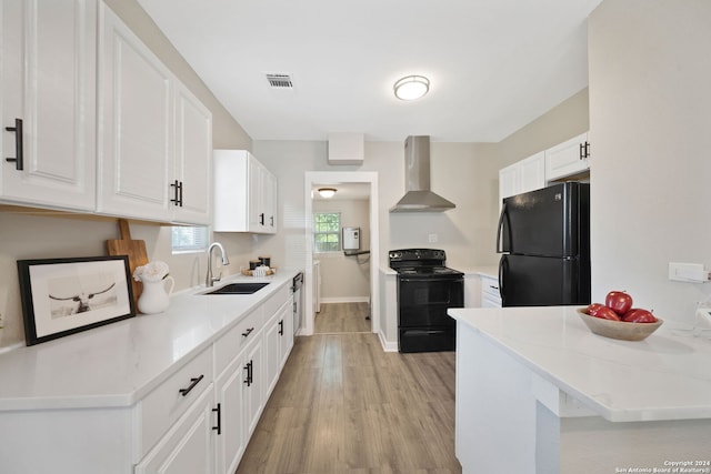 kitchen with visible vents, white cabinets, a sink, wall chimney range hood, and black appliances