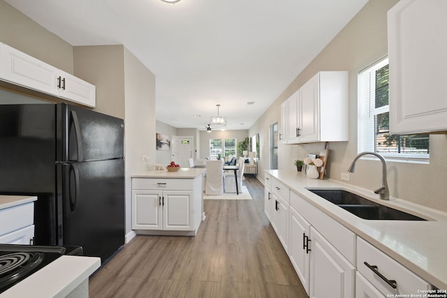 kitchen with black fridge, light hardwood / wood-style floors, white cabinets, sink, and kitchen peninsula