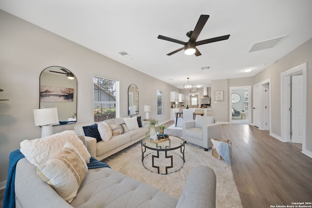 living area with ceiling fan with notable chandelier, light wood finished floors, visible vents, and baseboards