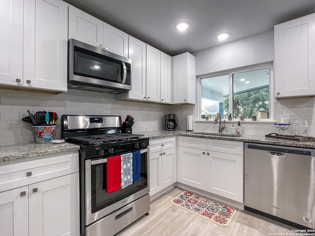 kitchen featuring appliances with stainless steel finishes, white cabinets, decorative backsplash, and light wood-type flooring