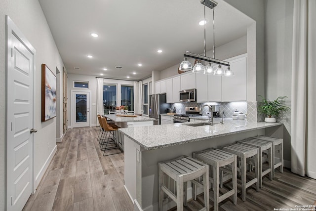 kitchen with kitchen peninsula, white cabinets, stainless steel appliances, light stone countertops, and pendant lighting