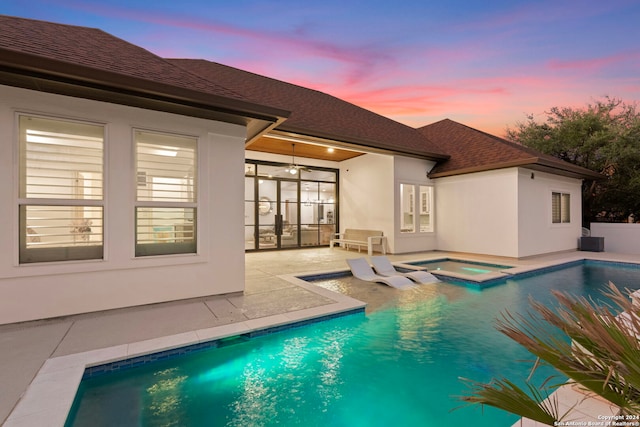 pool at dusk with a patio and an in ground hot tub