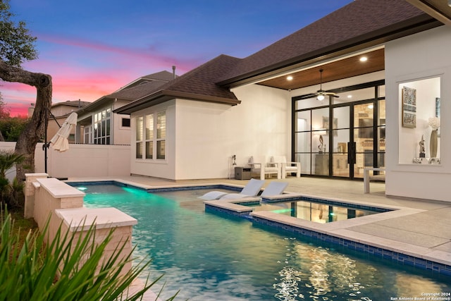 pool at dusk featuring an in ground hot tub, ceiling fan, and a patio