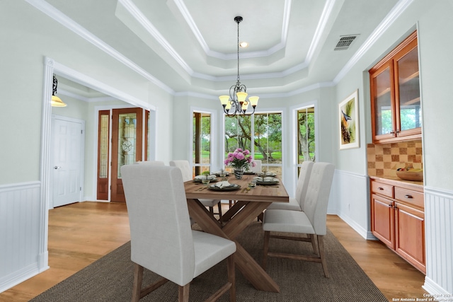 dining room featuring light hardwood / wood-style flooring, a chandelier, a tray ceiling, and ornamental molding