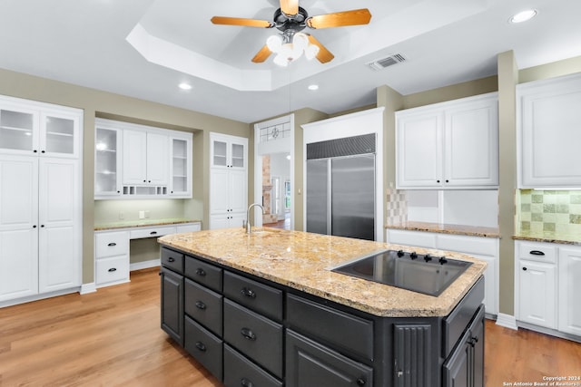 kitchen with black electric cooktop, tasteful backsplash, built in fridge, a raised ceiling, and a center island with sink