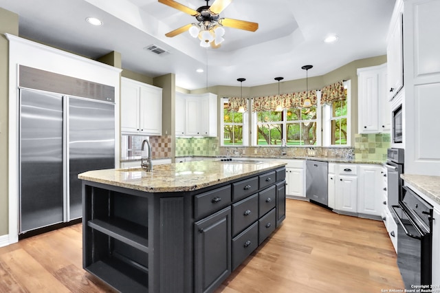 kitchen featuring decorative backsplash, light hardwood / wood-style floors, black appliances, and an island with sink