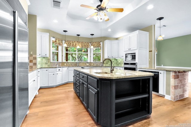 kitchen featuring built in appliances, white cabinetry, light wood-type flooring, and a center island with sink