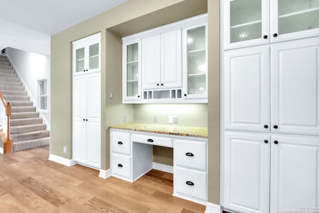 interior space with white cabinetry, light stone countertops, light hardwood / wood-style flooring, and built in desk