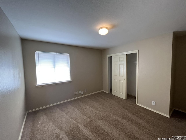 unfurnished bedroom with baseboards, dark carpet, and a closet