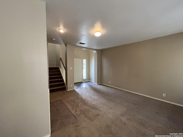 carpeted empty room with arched walkways, stairway, and baseboards