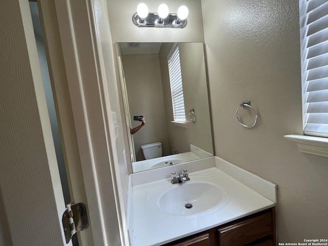 bathroom with toilet, a textured wall, and vanity