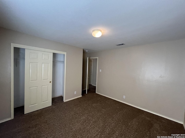 unfurnished bedroom with baseboards, visible vents, dark colored carpet, and a closet