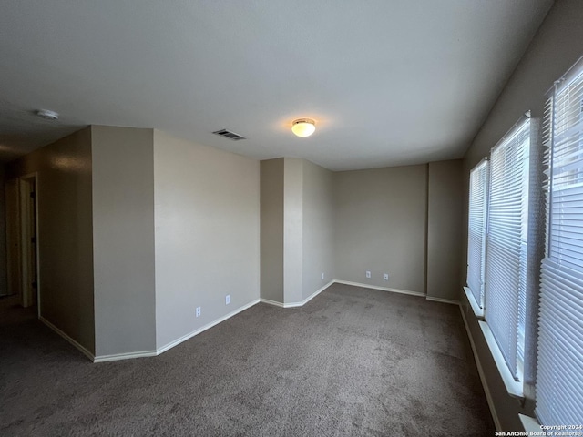 spare room with dark colored carpet, visible vents, and baseboards