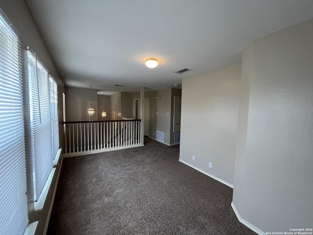 empty room featuring visible vents, dark carpet, and baseboards