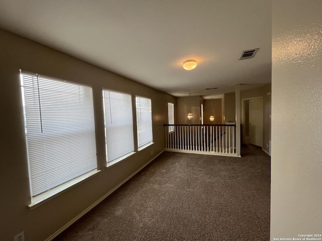 empty room with dark colored carpet, visible vents, and baseboards