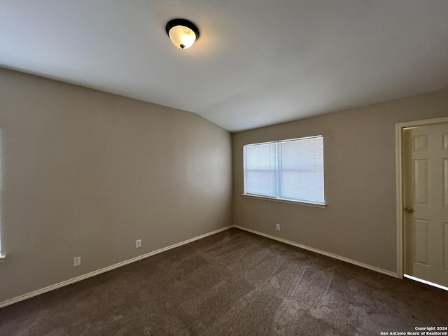 empty room featuring dark colored carpet, vaulted ceiling, and baseboards