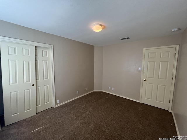 unfurnished bedroom featuring baseboards, visible vents, dark colored carpet, and a closet