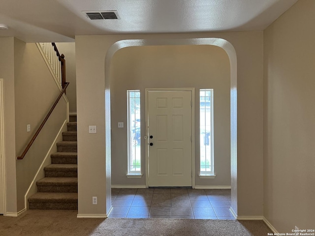 carpeted entryway with arched walkways, visible vents, baseboards, stairway, and tile patterned floors