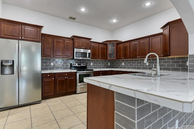 kitchen with sink, light tile patterned floors, appliances with stainless steel finishes, light stone countertops, and decorative backsplash