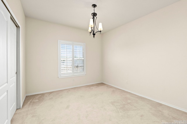 unfurnished room featuring an inviting chandelier, baseboards, and light colored carpet