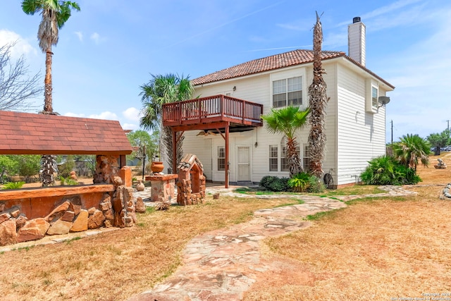 rear view of property with a wooden deck, a chimney, a tiled roof, a gazebo, and a yard