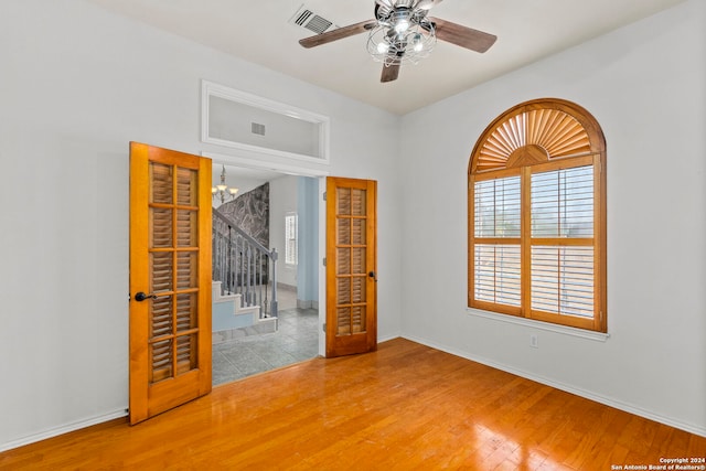 empty room with ceiling fan with notable chandelier, wood finished floors, visible vents, and baseboards