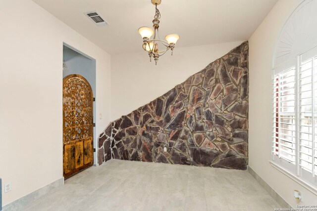 unfurnished dining area featuring a stone fireplace, light tile patterned flooring, and a notable chandelier