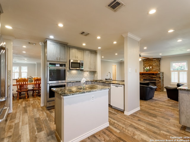 kitchen with appliances with stainless steel finishes, crown molding, dark stone countertops, light hardwood / wood-style floors, and a stone fireplace