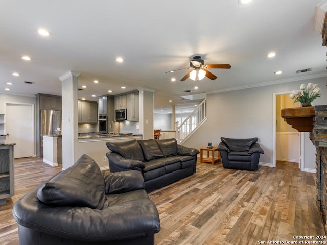 living area featuring ornamental molding, stairway, a stone fireplace, and light wood-style flooring