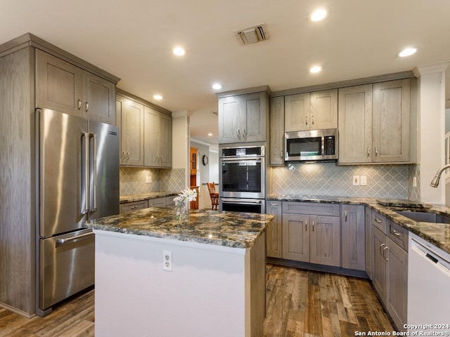 kitchen featuring visible vents, a kitchen island, appliances with stainless steel finishes, dark stone countertops, and a sink