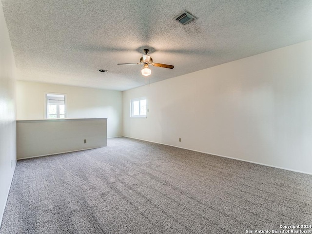 unfurnished room with a textured ceiling, carpet flooring, visible vents, and a ceiling fan