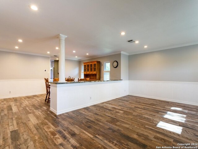 kitchen with a peninsula, ornate columns, dark stone countertops, and a wainscoted wall