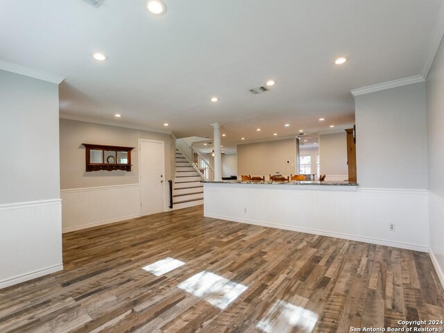 unfurnished living room featuring dark wood-type flooring, visible vents, stairway, wainscoting, and crown molding