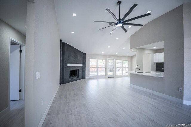 unfurnished living room with ceiling fan, lofted ceiling, light hardwood / wood-style flooring, and a large fireplace