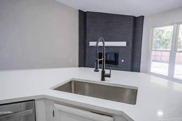 kitchen with sink, a fireplace, dishwasher, and white cabinets