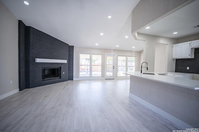 kitchen with sink, white cabinetry, vaulted ceiling, a brick fireplace, and light wood-type flooring