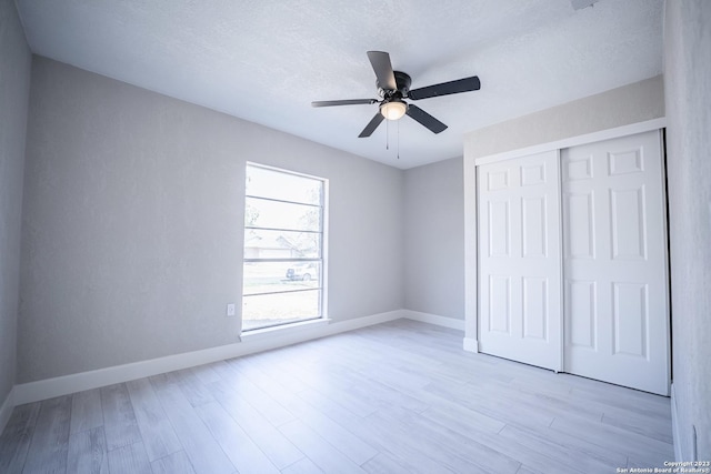 unfurnished bedroom featuring ceiling fan, a closet, a textured ceiling, and light wood-type flooring