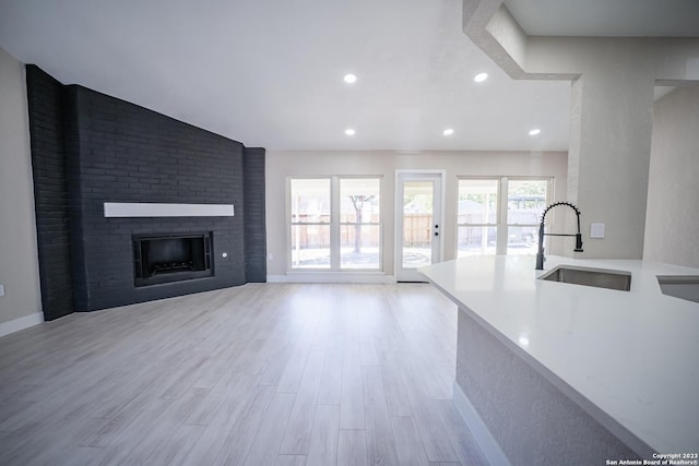 unfurnished living room with vaulted ceiling, sink, a fireplace, and light wood-type flooring