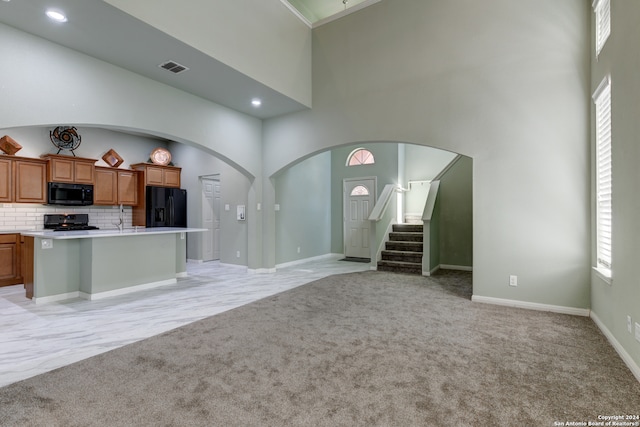 kitchen featuring black appliances, a kitchen bar, light colored carpet, a towering ceiling, and backsplash