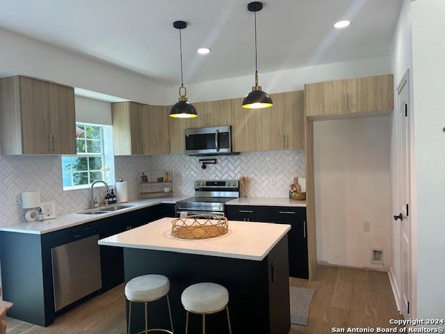 kitchen featuring sink, hanging light fixtures, stainless steel appliances, a center island, and light wood-type flooring