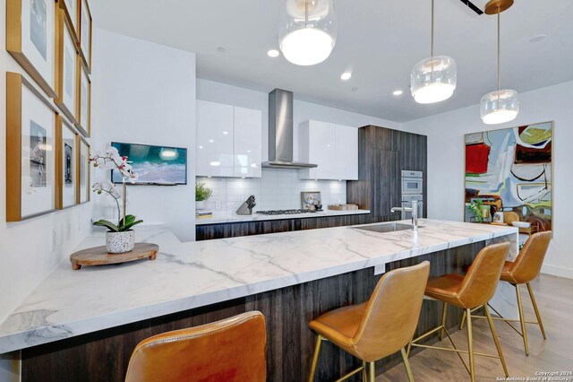 kitchen with a kitchen bar, tasteful backsplash, wall chimney range hood, dark brown cabinetry, and white cabinetry