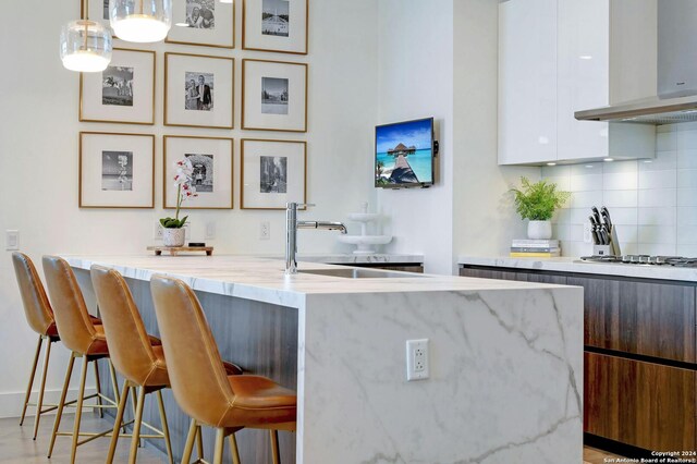 bar with white cabinetry, tasteful backsplash, wall chimney range hood, hanging light fixtures, and light hardwood / wood-style flooring