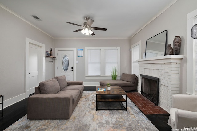 living room with a brick fireplace, dark wood-type flooring, ornamental molding, and ceiling fan